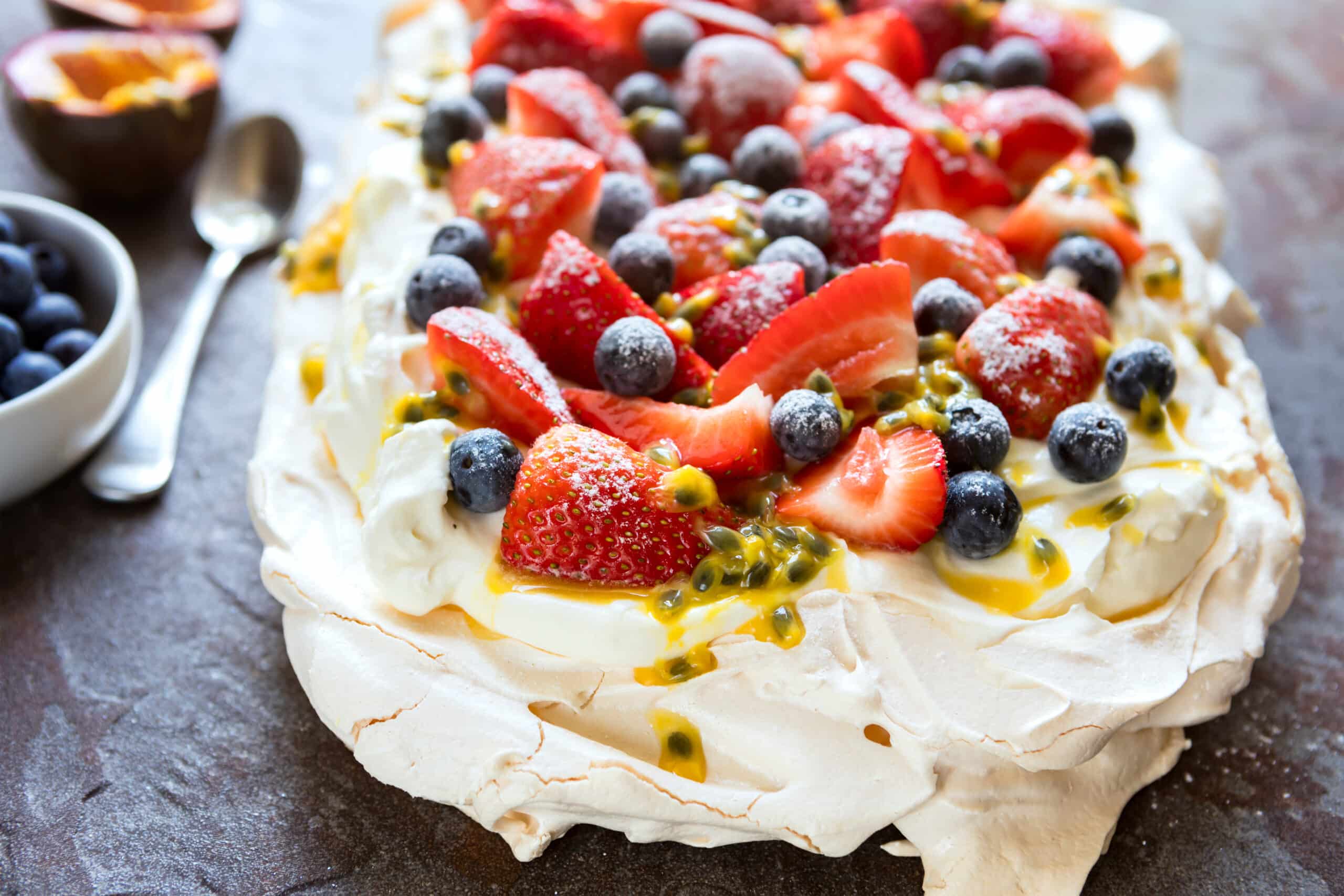 Pavlova croustillante garnie de crème, fraises, myrtilles et fruit de la passion saupoudrée de sucre glace.
